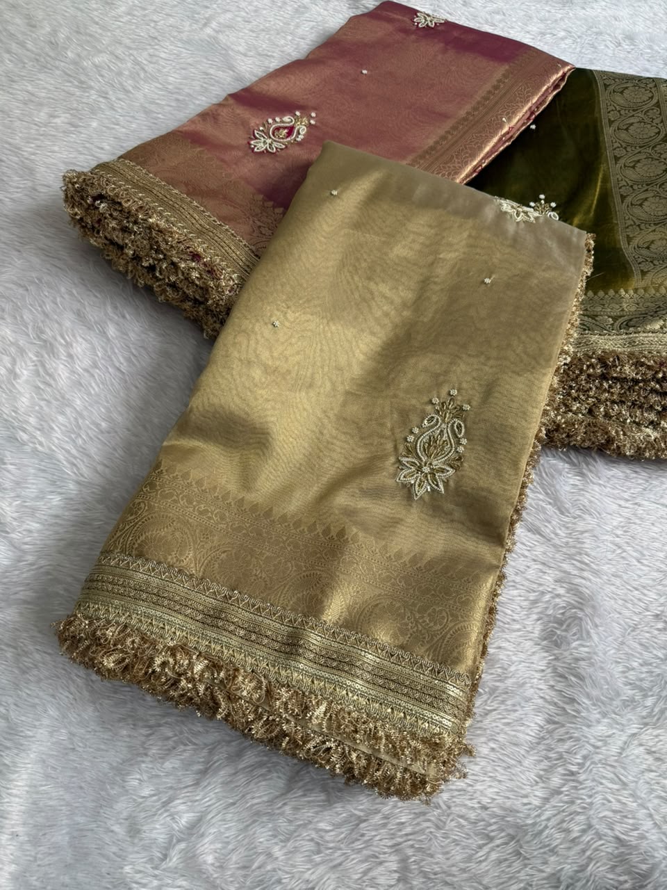 Gold tissue saree with zari border and embroidered motifs, folded with green inner panel