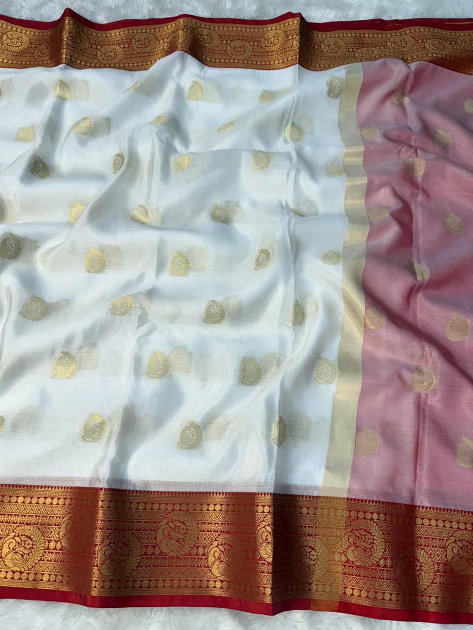 White tapeta saree laid flat with gold motifs, pink side panel, and red-gold border