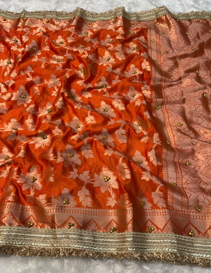 Orange silk saree with dense floral embroidery and gold fringe along the edge